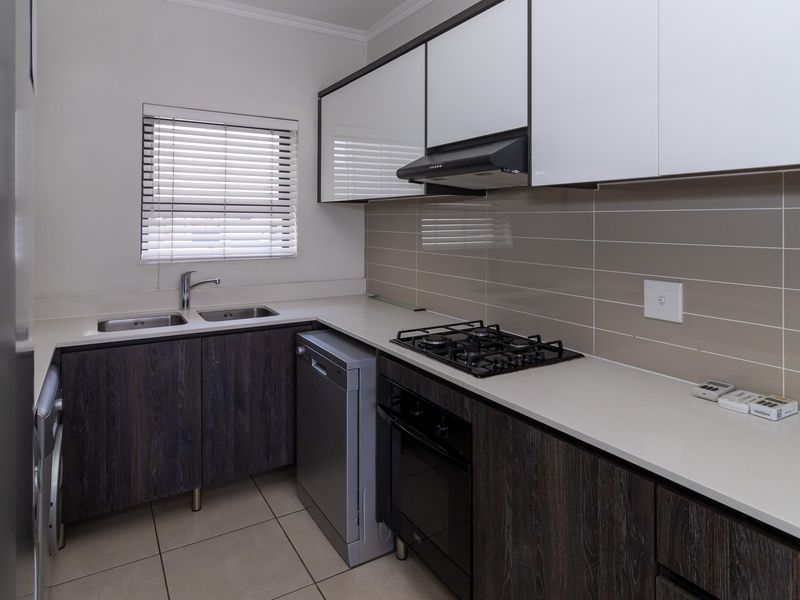 Modern kitchen featuring dark wood-grain lower cabinetry, white upper cabinets, stone countertops, gas hob, built-in oven, and a double sink with tiled backsplash.