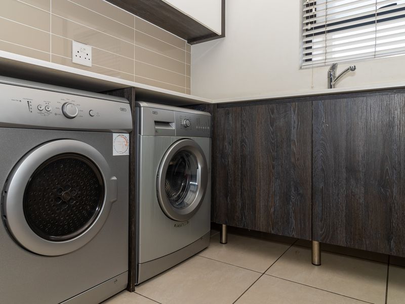 A functional laundry area featuring built-in dark wood cabinetry, tiled backsplash, a sink with faucet, and tiled flooring.