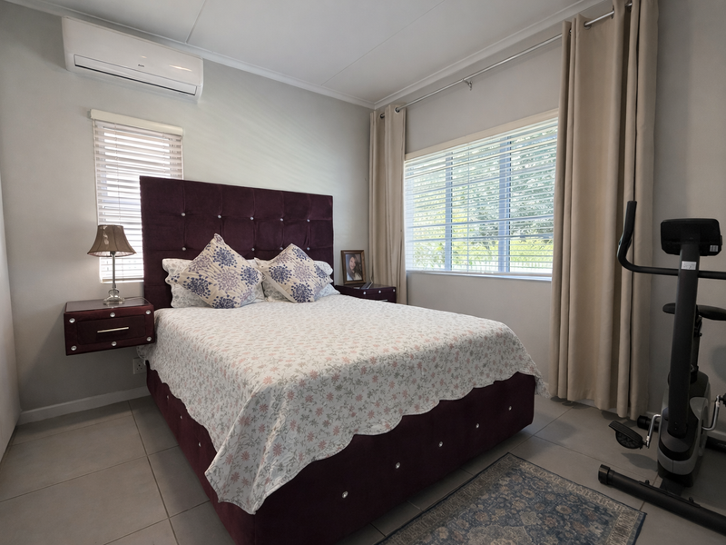 A well-maintained bedroom featuring tiled flooring, a built-in wardrobe, and a wall-mounted split-system air conditioner for climate control.
