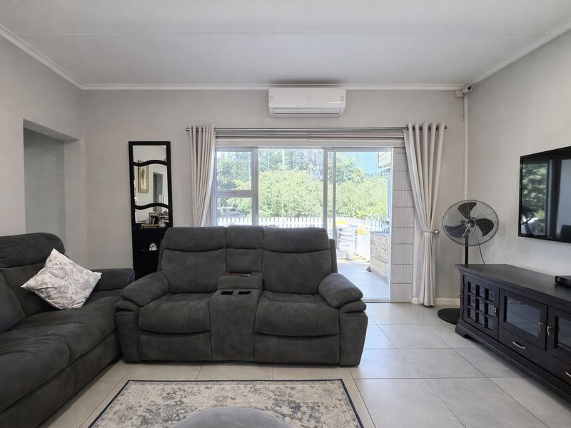 A well-maintained living room featuring tiled flooring, a split-system air conditioner, and a large sliding glass door providing access to the outdoor area.