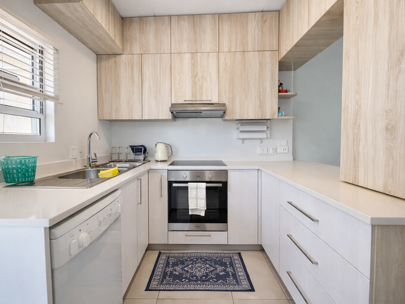 Modern kitchen featuring light wood-grain cabinetry, stone countertops, integrated oven, hob, and extractor fan, with ample storage and a bright window.