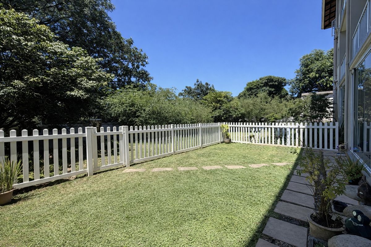 A well-maintained rear garden featuring a white picket fence, a stone paver walkway, and a manicured lawn area.