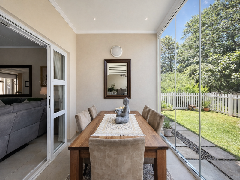 A bright, enclosed patio featuring full-height glass walls, tiled flooring, and recessed lighting, offering a seamless transition to the garden area.