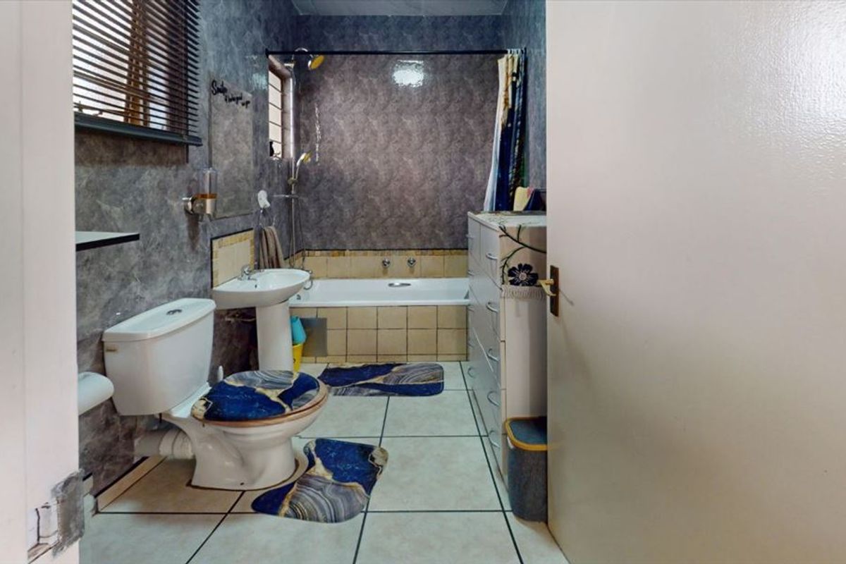 A functional bathroom featuring a pedestal basin, toilet, and a built-in bathtub with shower attachment, finished with tiled walls and flooring.