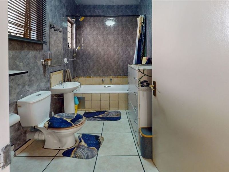 A functional bathroom featuring a pedestal basin, toilet, and a built-in bathtub with shower attachment, finished with tiled walls and flooring.