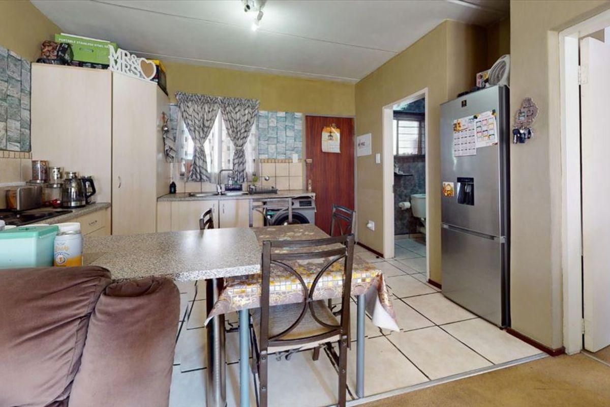 Open-plan kitchen area featuring built-in cabinetry, tiled flooring, and a tiled backsplash, with direct access to an adjacent bathroom.