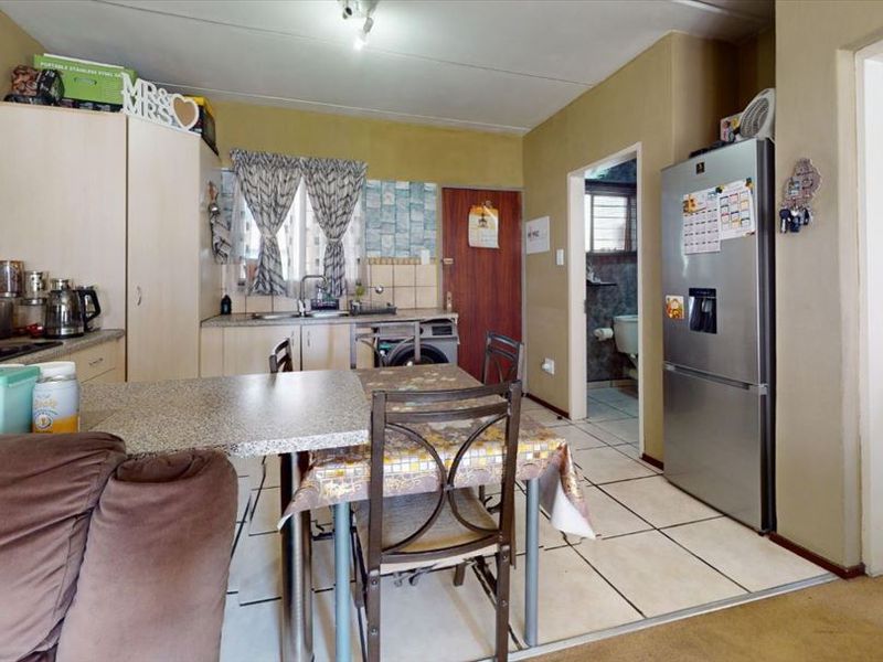 Open-plan kitchen area featuring built-in cabinetry, tiled flooring, and a tiled backsplash, with direct access to an adjacent bathroom.