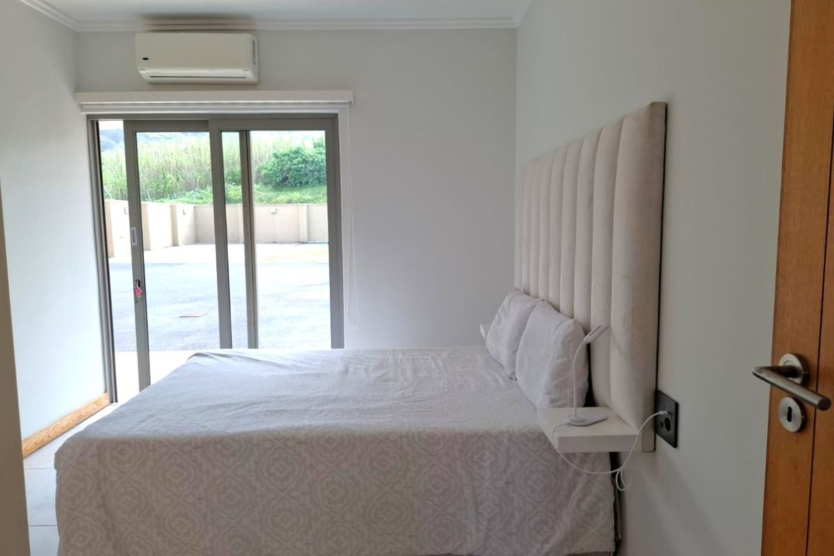 A well-maintained bedroom featuring a built-in headboard, floating bedside shelf, split-system air conditioning, and a sliding glass door providing access to the exterior.