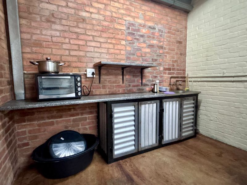 A rustic scullery area featuring exposed brick walls, stone countertops, and industrial-style metal cabinetry with an integrated sink.