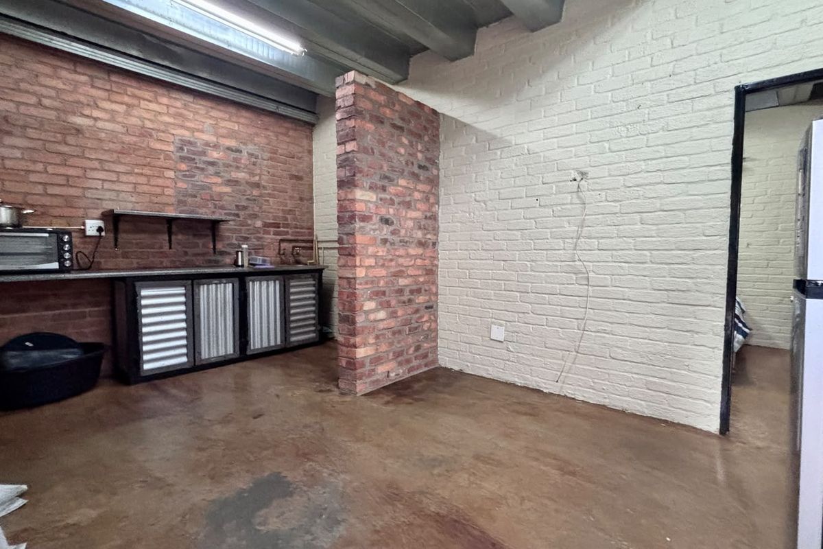 Industrial-style kitchen area featuring exposed brick walls, concrete flooring, and basic built-in cabinetry with an open-plan layout.