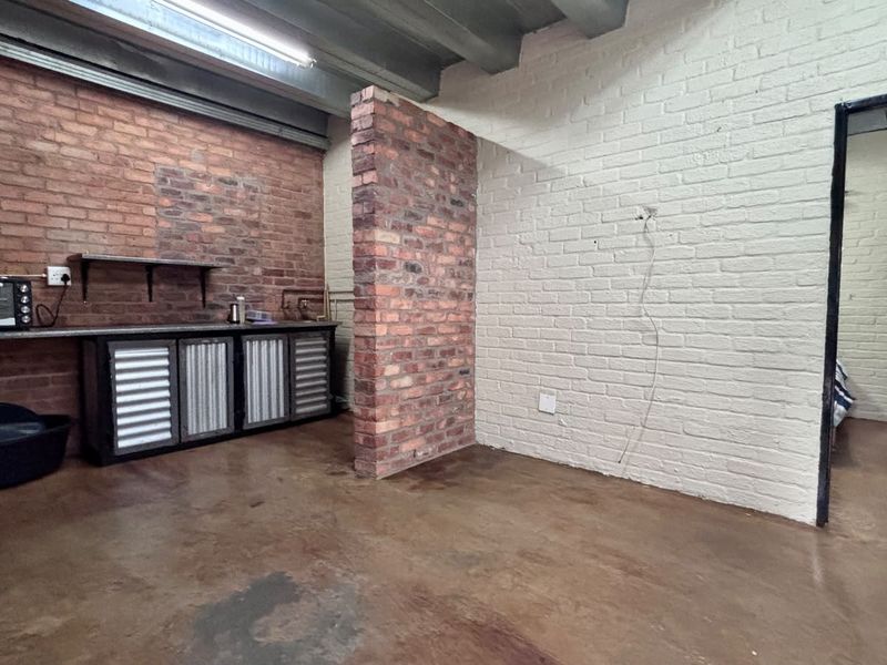 Industrial-style kitchen area featuring exposed brick walls, concrete flooring, and basic built-in cabinetry with an open-plan layout.