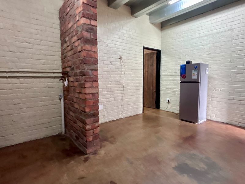 An open-plan industrial style space featuring exposed brickwork, painted brick walls, exposed ceiling beams, and concrete flooring.
