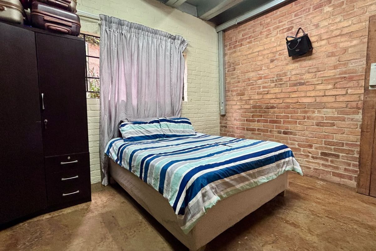 Bedroom featuring an industrial aesthetic with exposed brick walls, painted brick accents, and exposed ceiling beams.