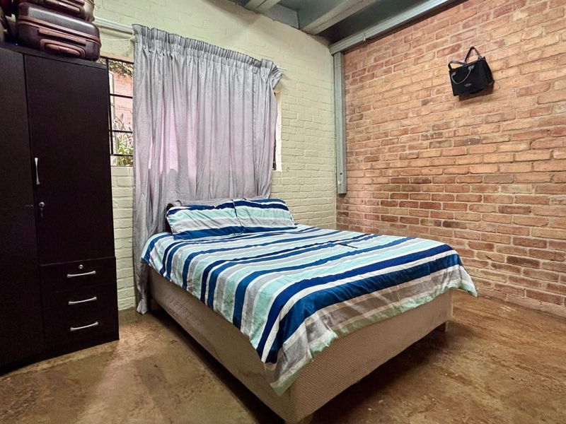 Bedroom featuring an industrial aesthetic with exposed brick walls, painted brick accents, and exposed ceiling beams.