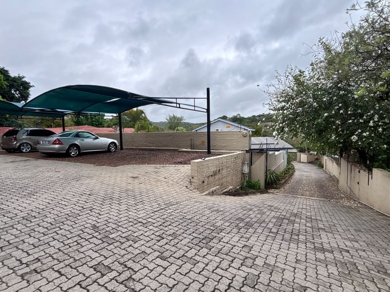 Exterior view of the property featuring a paved driveway, a covered carport area, and perimeter boundary walls.