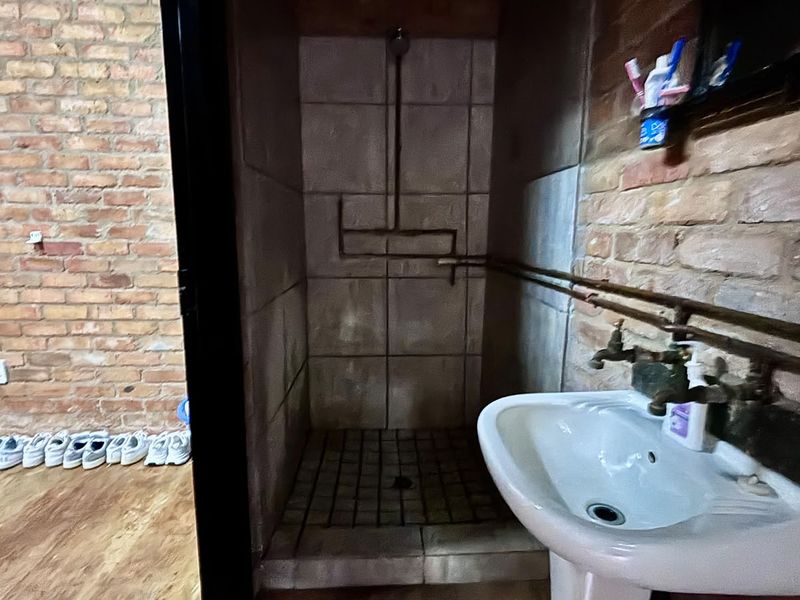A rustic-style bathroom featuring exposed brick walls, a pedestal basin, and an open tiled shower area with exposed copper plumbing fixtures.