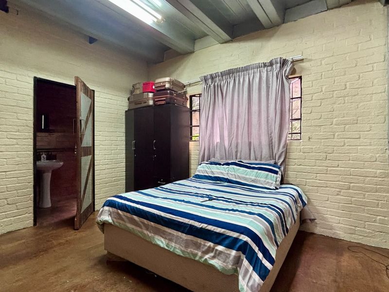 Bedroom featuring exposed brick walls and ceiling beams, with an adjoining bathroom entrance.