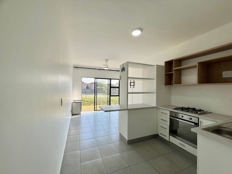 Modern open-plan kitchen and living area featuring tiled floors, built-in cabinetry, gas hob, oven, and direct access to an outdoor space via sliding doors.
