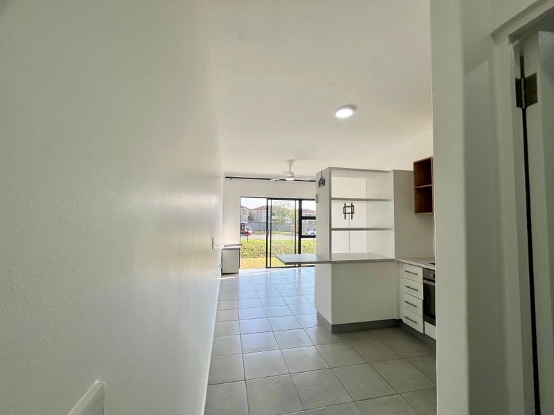 An open-plan living and kitchen area featuring tiled flooring, built-in cabinetry, a breakfast bar, and a sliding glass door leading to the exterior.