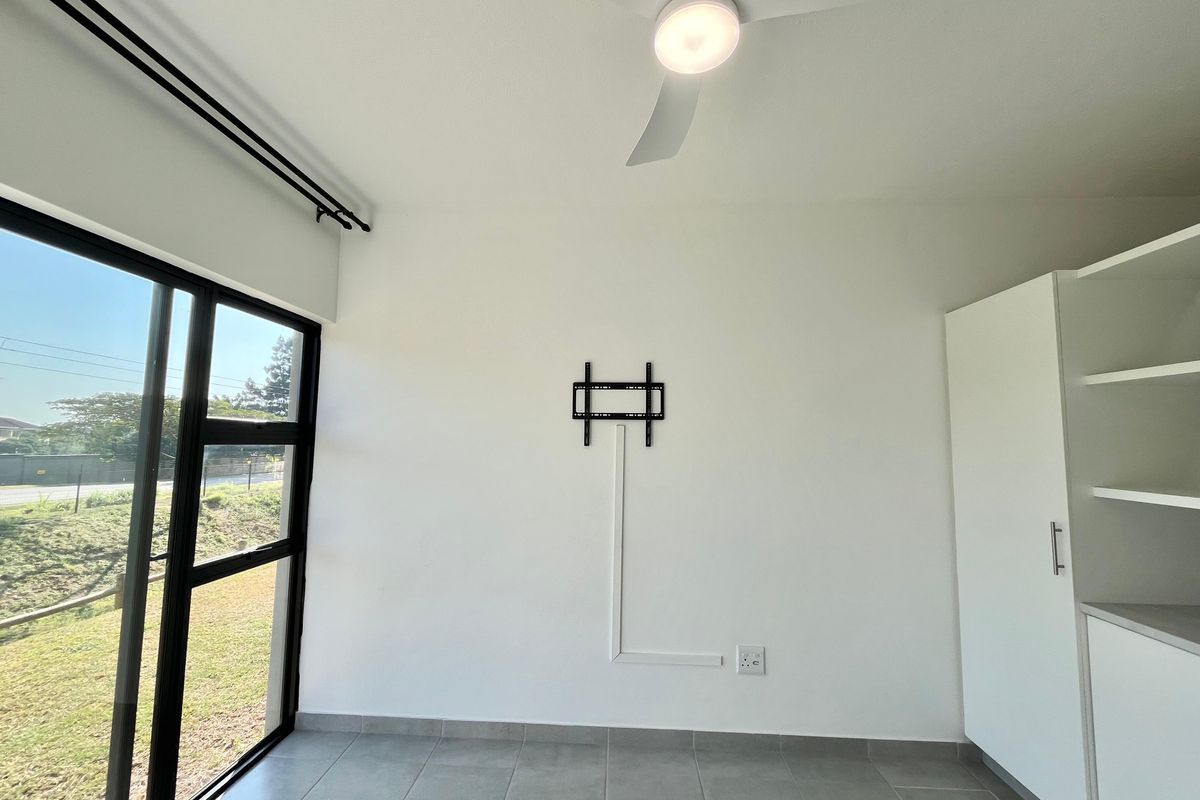 A bright, empty living area featuring tiled floors, a ceiling fan, built-in storage cabinetry, and a sliding glass door leading outdoors.
