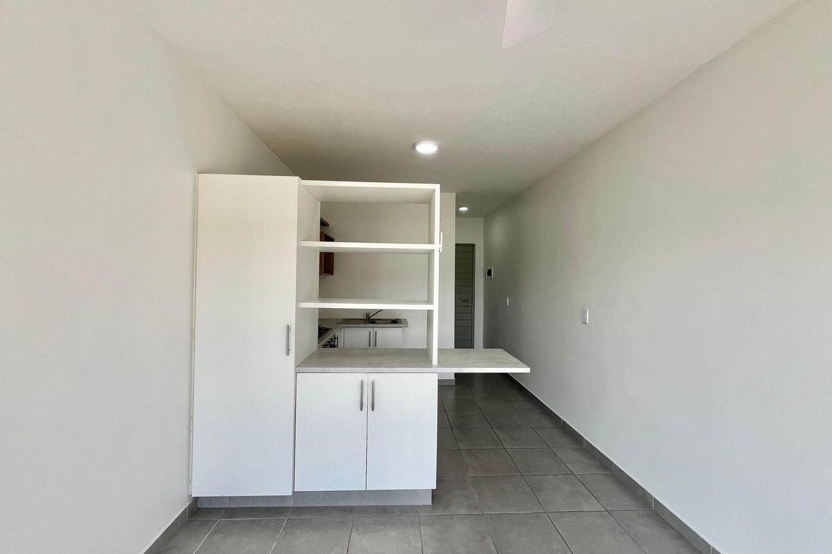 A clean, minimalist kitchen area featuring white built-in cabinetry, a sink, and neutral tiled flooring in an open-plan layout.