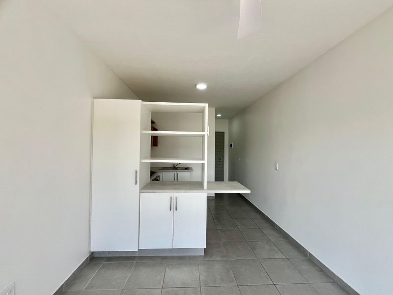 A clean, minimalist kitchen area featuring white built-in cabinetry, a sink, and neutral tiled flooring in an open-plan layout.