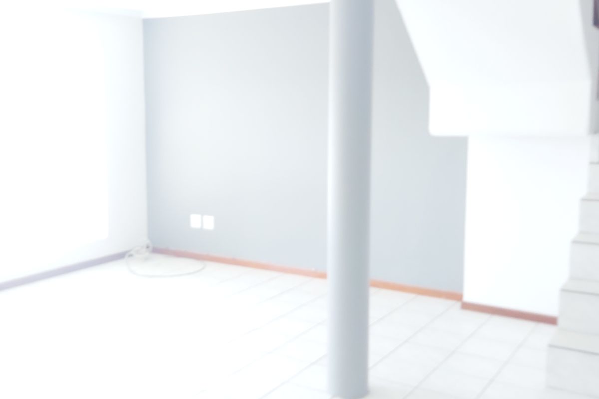 An empty, open-plan living area featuring tiled flooring, a central structural column, and an integrated staircase.