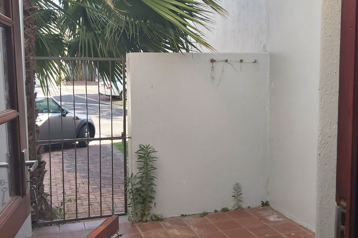 A small outdoor patio area featuring tiled flooring and a metal security gate, providing access to the front driveway.