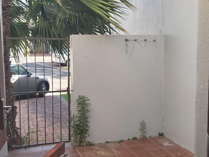 A small outdoor patio area featuring tiled flooring and a metal security gate, providing access to the front driveway.