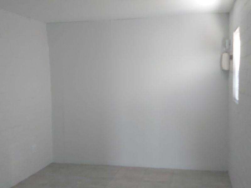 An empty, neutral-toned room featuring painted brick walls and tiled flooring, offering a blank canvas for potential bedroom or office use.