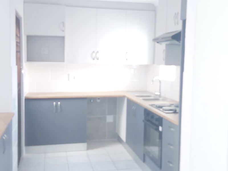 A bright, modern kitchen featuring two-tone cabinetry, wood-look countertops, built-in oven, hob, and extractor fan with tiled flooring.