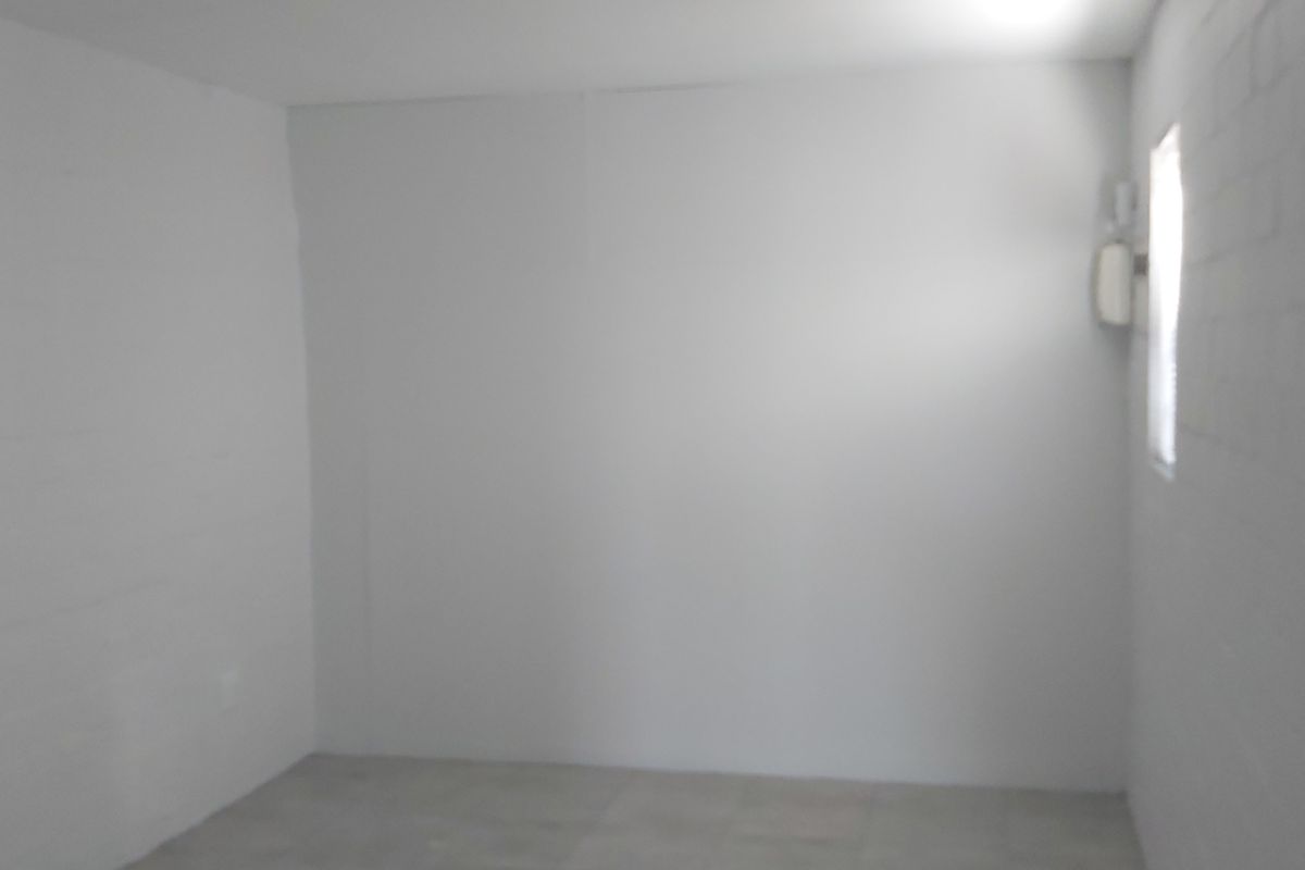 An empty, neutral-toned room featuring painted brick walls and tiled flooring, offering a blank canvas for potential bedroom or office use.