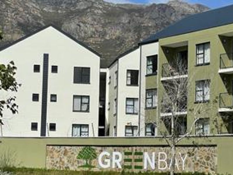 Modern multi-story apartment complex featuring contemporary architecture, private balconies, and a prominent stone-clad entrance signage wall set against a mountain backdrop.