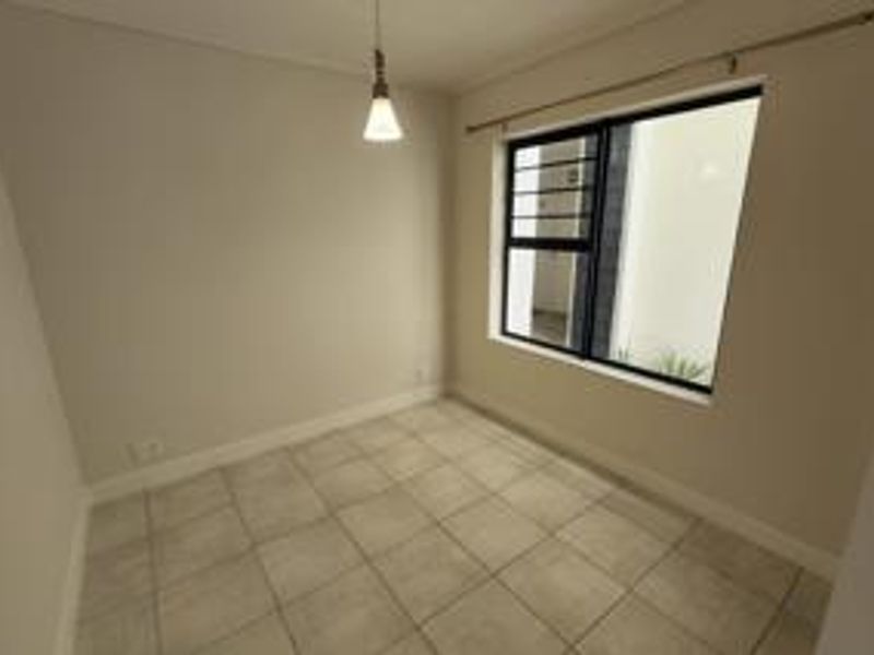 A clean, empty bedroom featuring neutral tiled flooring, a pendant light fixture, and a window fitted with security bars and a curtain rod.