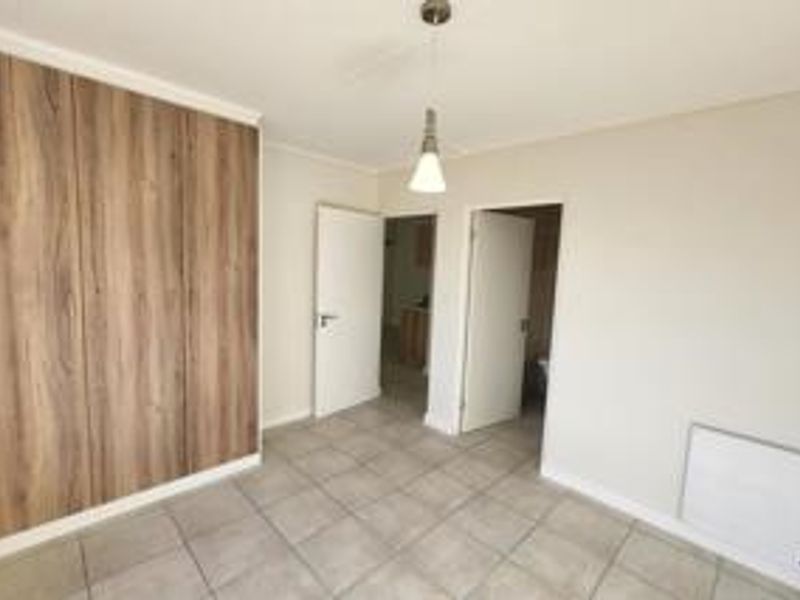 A bright, empty bedroom featuring modern wood-finish built-in cupboards, neutral tiled flooring, and a wall-mounted heater.