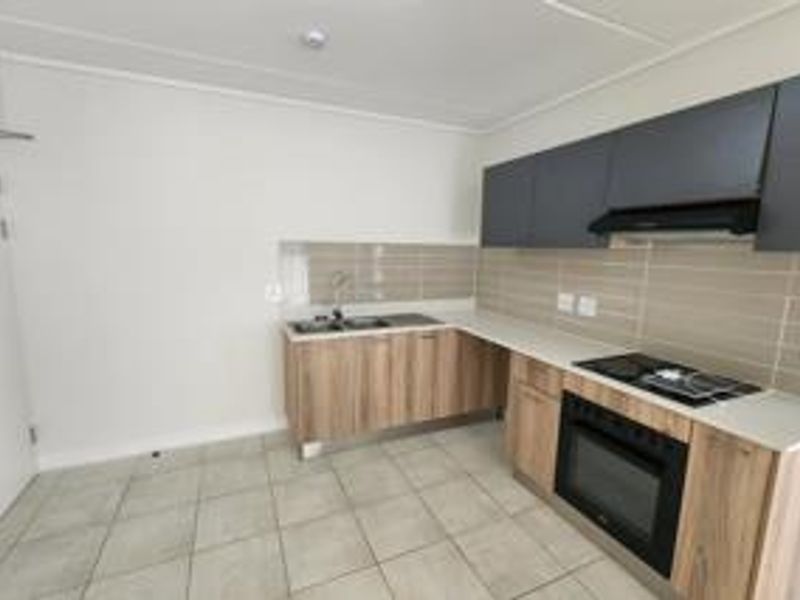 Modern kitchen featuring wood-finish lower cabinetry, dark upper cabinets, integrated oven and hob, and neutral tiled backsplash.
