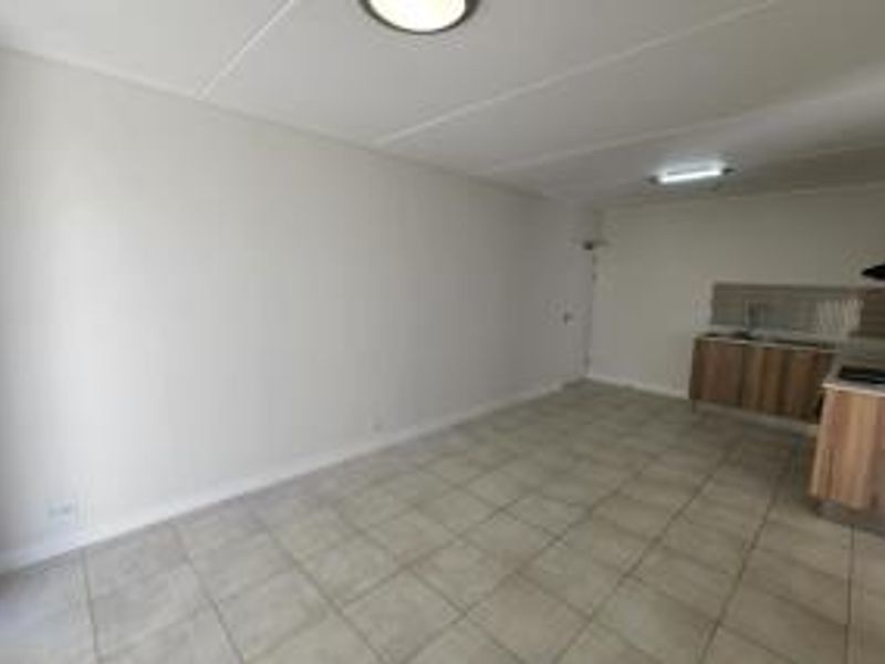 An open-plan living and kitchen area featuring tiled flooring, neutral walls, and functional kitchen cabinetry with an integrated extractor fan.
