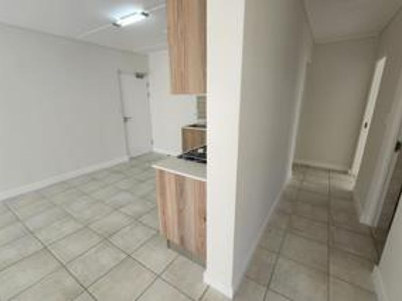 An open-plan living and kitchen area featuring tiled flooring, built-in cabinetry, and a hob, presented in a clean, vacant condition.