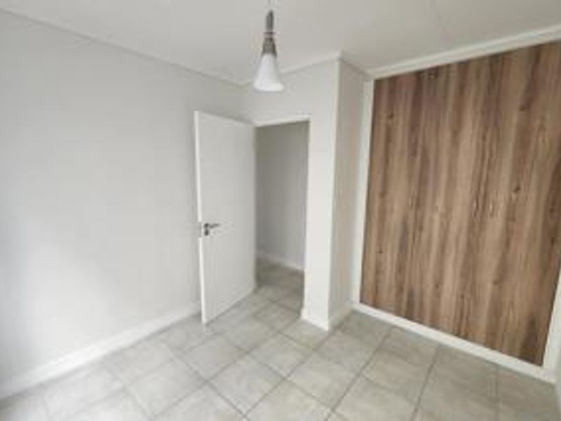 A clean, empty bedroom featuring modern wood-finish built-in cupboards, neutral tiled flooring, and a simple pendant light fixture.