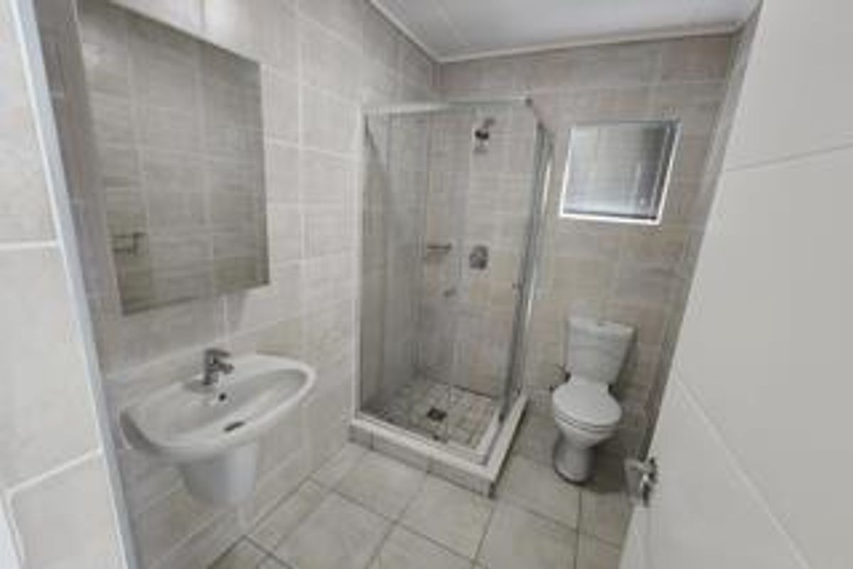 A clean, modern bathroom featuring a glass shower enclosure, pedestal basin, and toilet with neutral wall and floor tiling.