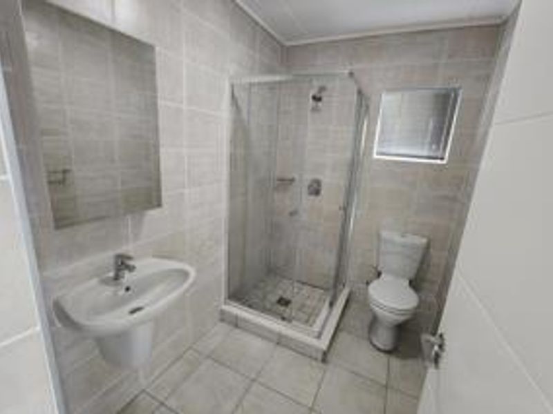 A clean, modern bathroom featuring a glass shower enclosure, pedestal basin, and toilet with neutral wall and floor tiling.