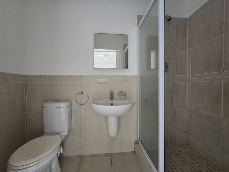 A functional bathroom featuring a pedestal washbasin, toilet, and a glass-enclosed shower with neutral wall and floor tiling.