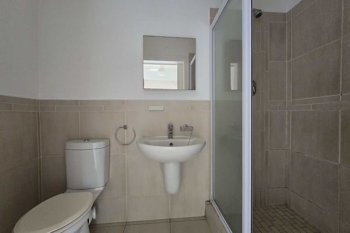 A functional bathroom featuring a pedestal washbasin, toilet, and a glass-enclosed shower with neutral wall and floor tiling.