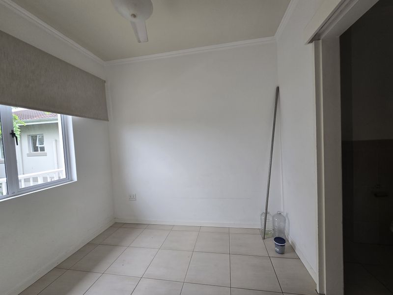 A vacant bedroom featuring neutral tiled flooring, a ceiling fan, and a roller blind, offering a clean and versatile space.
