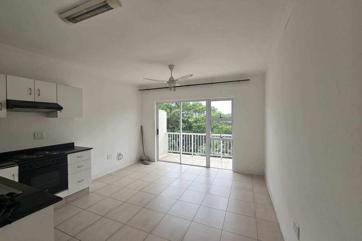 Open-plan kitchen and living area featuring tiled floors, built-in cabinetry, and a sliding door leading to a balcony with green views.