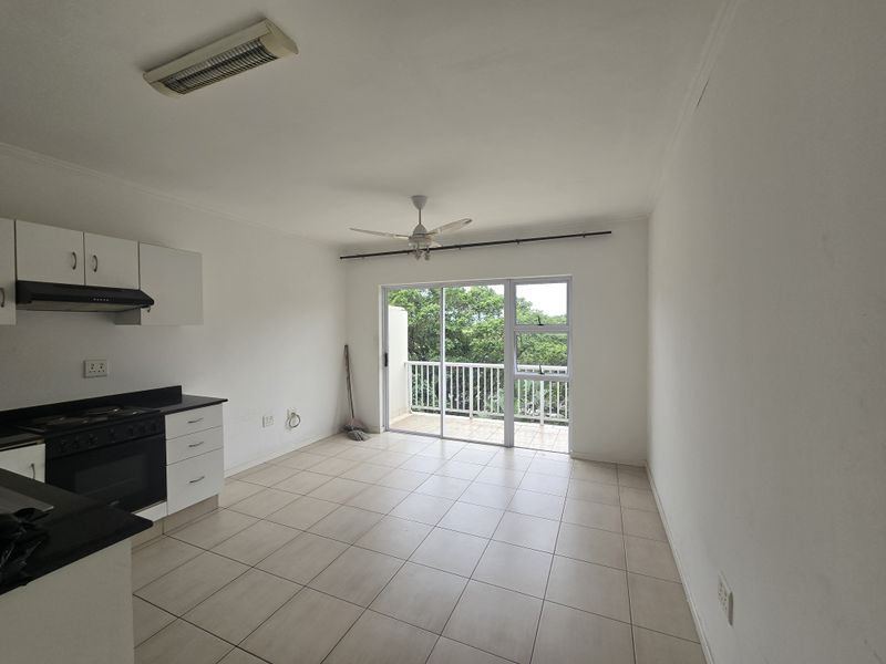 Open-plan kitchen and living area featuring tiled floors, built-in cabinetry, and a sliding door leading to a balcony with green views.