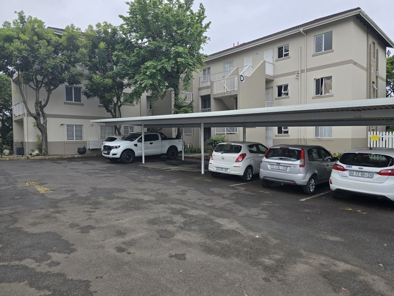 Exterior view of a multi-story apartment complex featuring a paved parking area with covered carports and building access via external stairwells.