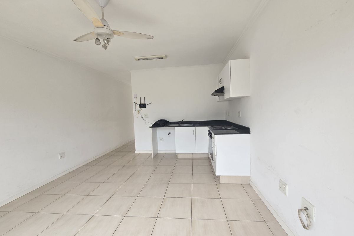 An open-plan living and kitchen area featuring tiled flooring, a ceiling fan, and basic built-in kitchen cabinetry with an integrated hob and oven.