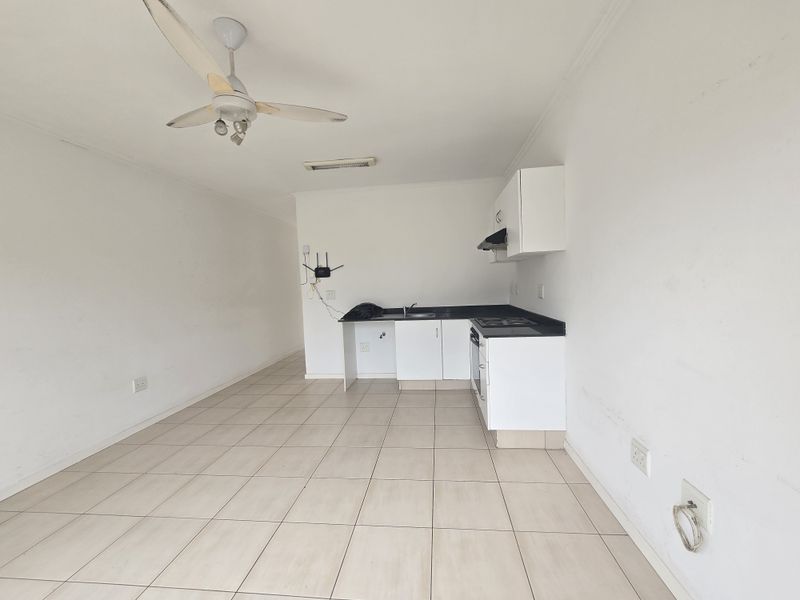 An open-plan living and kitchen area featuring tiled flooring, a ceiling fan, and basic built-in kitchen cabinetry with an integrated hob and oven.