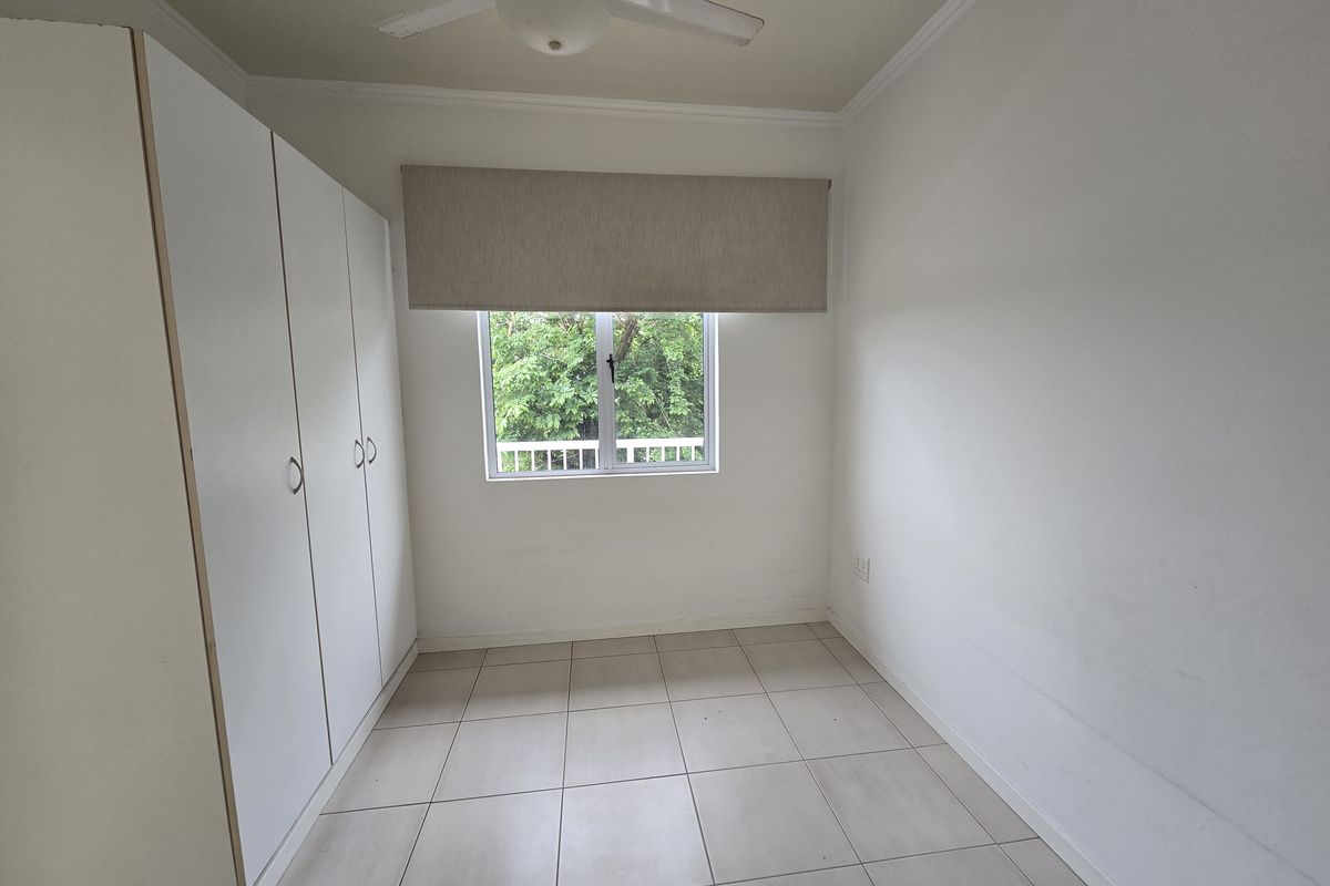 A bright, empty bedroom featuring neutral tiled flooring, built-in cupboards, and a ceiling fan, offering a clean canvas for personalization.